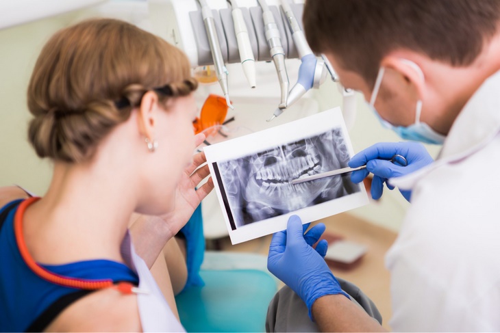 Врач-стоматолог демонстрирует пациентке рентгеновский снимок